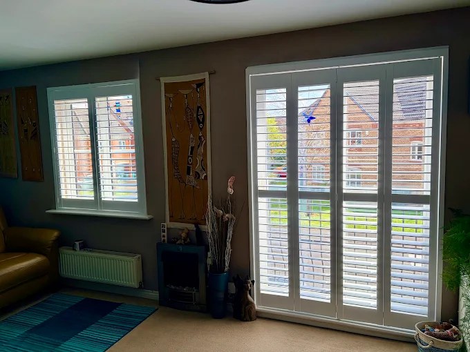 White plantation shutters fitted to a living room window and patio doors by Greystone Shutters